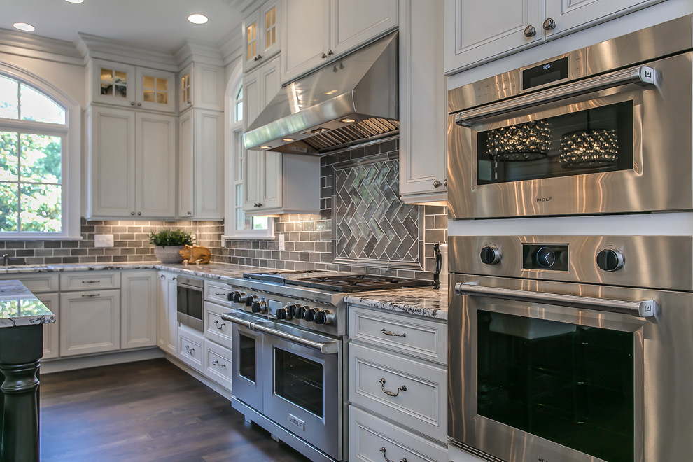 Exempel på ett stort klassiskt flerfärgad flerfärgat kök och matrum, med släta luckor, vita skåp, granitbänkskiva, grått stänkskydd, stänkskydd i glaskakel, rostfria vitvaror, mörkt trägolv, en köksö och brunt golv