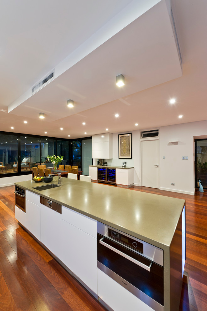 Design ideas for an expansive contemporary kitchen/diner in Perth with a submerged sink, flat-panel cabinets, white cabinets, composite countertops, metallic splashback, glass sheet splashback, dark hardwood flooring and an island.