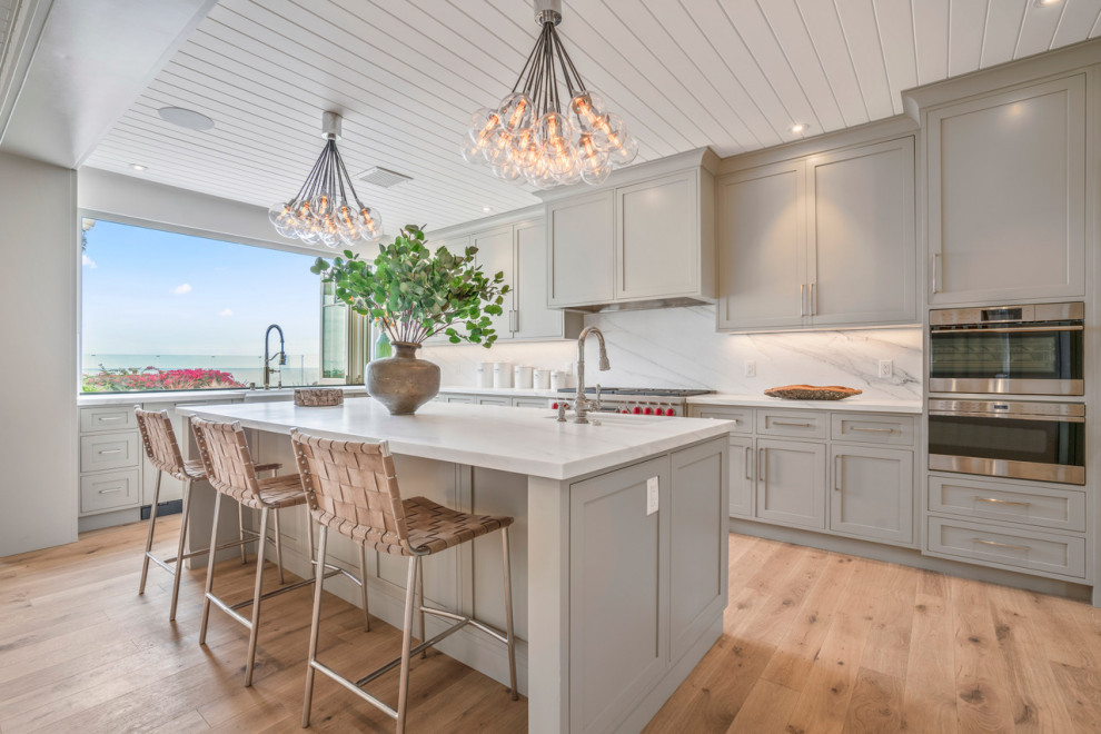 Traditional galley kitchen in New York with a submerged sink, shaker cabinets, grey cabinets, white splashback, stainless steel appliances, light hardwood flooring, an island, beige floors, white worktops and a timber clad ceiling.
