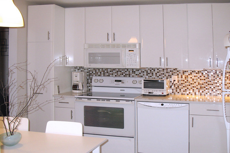 Cette photo montre une petite cuisine tendance en L avec un placard à porte plane et des portes de placard blanches.