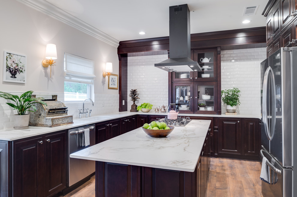 Photo of a large traditional u-shaped enclosed kitchen in New York with a single-bowl sink, raised-panel cabinets, dark wood cabinets, marble worktops, white splashback, metro tiled splashback, stainless steel appliances, medium hardwood flooring, an island and brown floors.