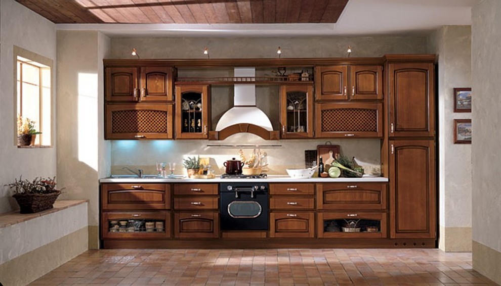 マイアミにある小さな地中海スタイルのおしゃれなキッチン (レイズドパネル扉のキャビネット、中間色木目調キャビネット、パネルと同色の調理設備、レンガの床、アイランドなし) の写真