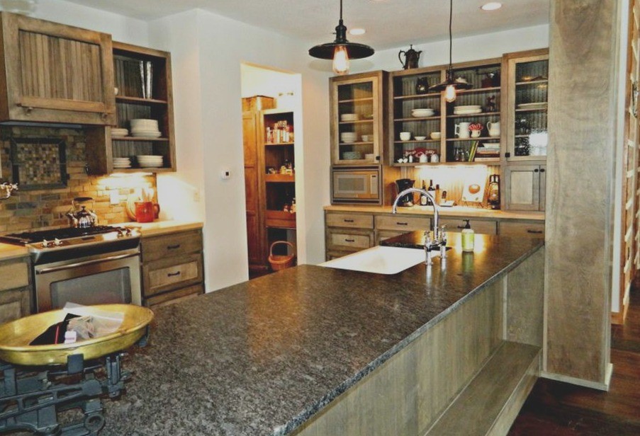 Example of a mid-sized mountain style galley dark wood floor eat-in kitchen design in Minneapolis with a farmhouse sink, glass-front cabinets, gray cabinets, granite countertops, gray backsplash, stone tile backsplash, stainless steel appliances and an island