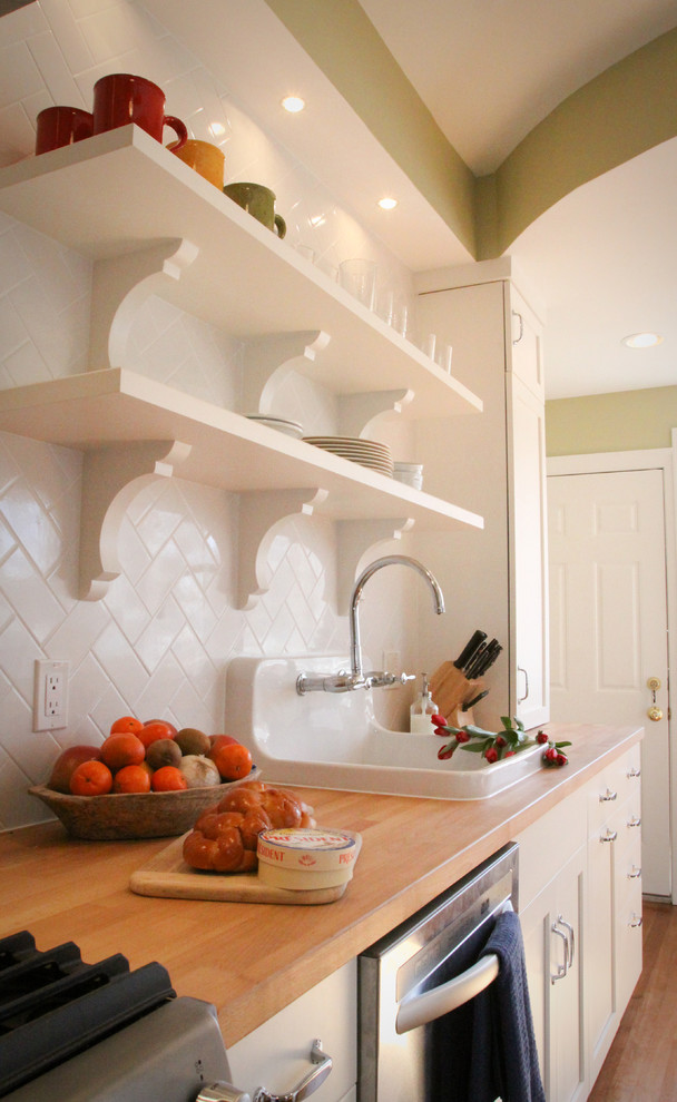 Enclosed kitchen - mid-sized traditional galley medium tone wood floor enclosed kitchen idea in DC Metro with a drop-in sink, open cabinets, white cabinets, wood countertops, white backsplash, subway tile backsplash, stainless steel appliances and no island