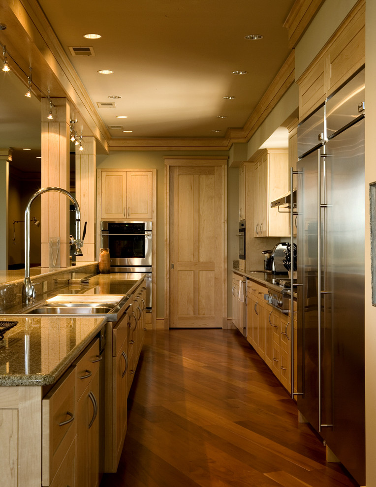 Ejemplo de cocina contemporánea con electrodomésticos de acero inoxidable, armarios con paneles empotrados y puertas de armario de madera clara