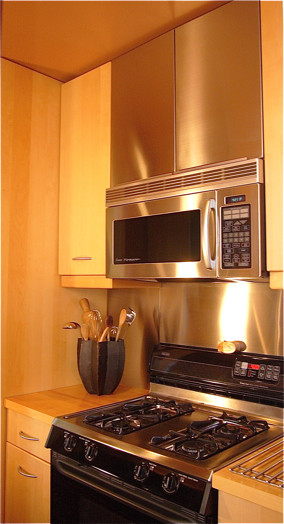 サンフランシスコにある低価格のコンテンポラリースタイルのおしゃれなキッチン (ドロップインシンク、フラットパネル扉のキャビネット、淡色木目調キャビネット、木材カウンター、メタリックのキッチンパネル、メタルタイルのキッチンパネル、黒い調理設備) の写真