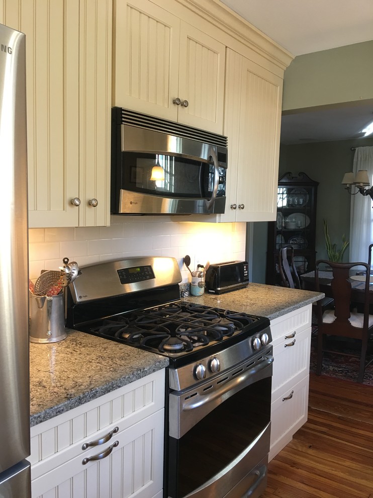 Photo of a small classic galley enclosed kitchen in Philadelphia with a submerged sink, flat-panel cabinets, yellow cabinets, engineered stone countertops, white splashback, ceramic splashback, stainless steel appliances, light hardwood flooring and no island.