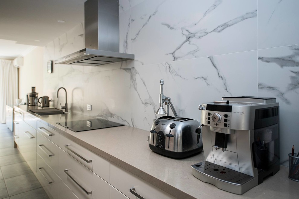 Mid-sized trendy galley porcelain tile and gray floor kitchen photo in Sydney with a double-bowl sink, flat-panel cabinets, white cabinets, quartz countertops, white backsplash, ceramic backsplash, stainless steel appliances, no island and beige countertops