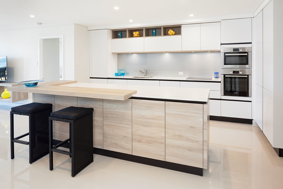 Moderne Küche mit flächenbündigen Schrankfronten, weißen Schränken, Küchenrückwand in Grau, Kücheninsel, Unterbauwaschbecken, Glasrückwand und Küchengeräten aus Edelstahl in Perth
