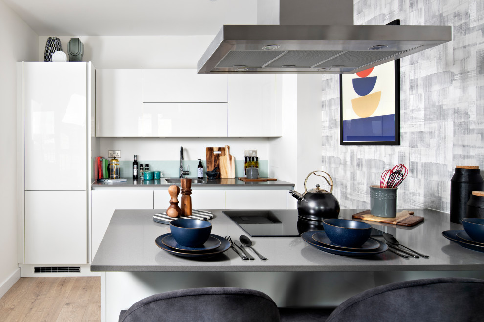 Inspiration för mellanstora moderna grått kök, med en enkel diskho, släta luckor, vita skåp, vitt stänkskydd, glaspanel som stänkskydd, integrerade vitvaror, ljust trägolv, en halv köksö och beiget golv