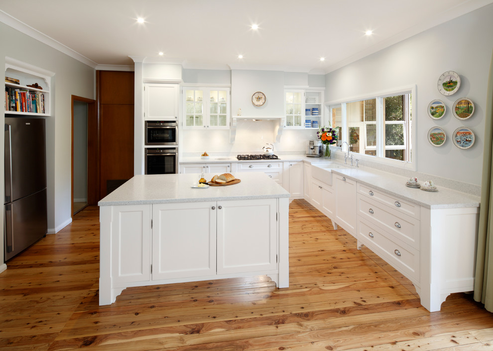 Example of a large classic l-shaped medium tone wood floor open concept kitchen design in Sydney with a double-bowl sink, recessed-panel cabinets, white cabinets, quartz countertops, white backsplash, ceramic backsplash, stainless steel appliances and an island