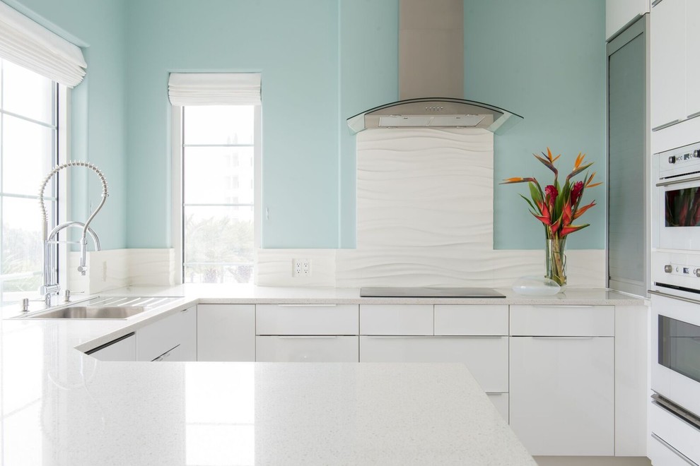 Mid-sized beach style u-shaped limestone floor kitchen photo in Houston with a single-bowl sink, flat-panel cabinets, white cabinets, white backsplash, white appliances, a peninsula and quartz countertops