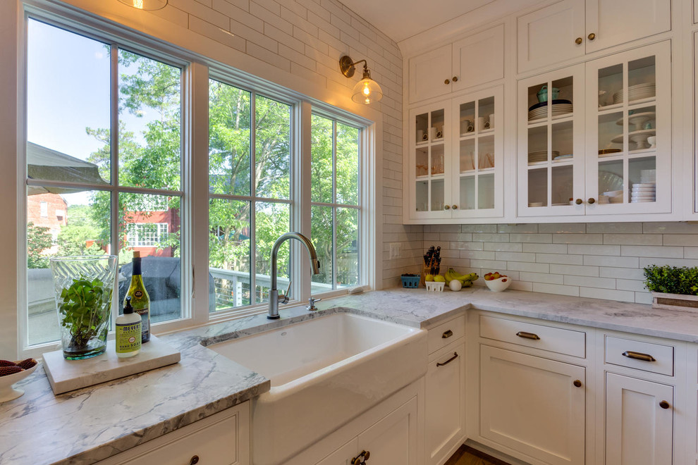 Diseño de cocina de estilo americano, de tamaño medio, con fregadero bajoencimera, puertas de armario blancas, encimera de mármol, salpicadero blanco, salpicadero de azulejos de cerámica, electrodomésticos de acero inoxidable, suelo de madera en tonos medios, una isla y armarios estilo shaker
