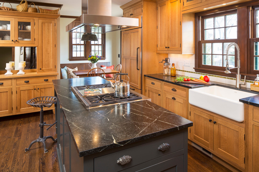 Inspiration for a mid-sized farmhouse l-shaped dark wood floor and brown floor open concept kitchen remodel in Minneapolis with a farmhouse sink, flat-panel cabinets, soapstone countertops, white backsplash, subway tile backsplash, an island, medium tone wood cabinets and paneled appliances