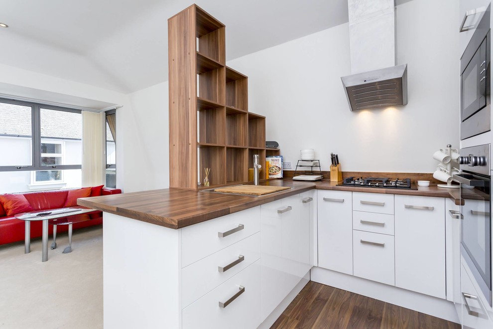 Kleine Moderne Küche in U-Form mit flächenbündigen Schrankfronten, weißen Schränken, Arbeitsplatte aus Holz, dunklem Holzboden und Halbinsel in Hampshire