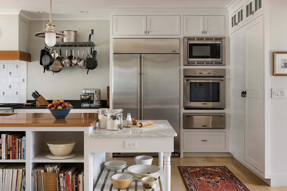 Inspiration for a mid-sized farmhouse u-shaped light wood floor and beige floor open concept kitchen remodel in Bridgeport with a farmhouse sink, shaker cabinets, white cabinets, granite countertops, white backsplash, porcelain backsplash, stainless steel appliances and an island