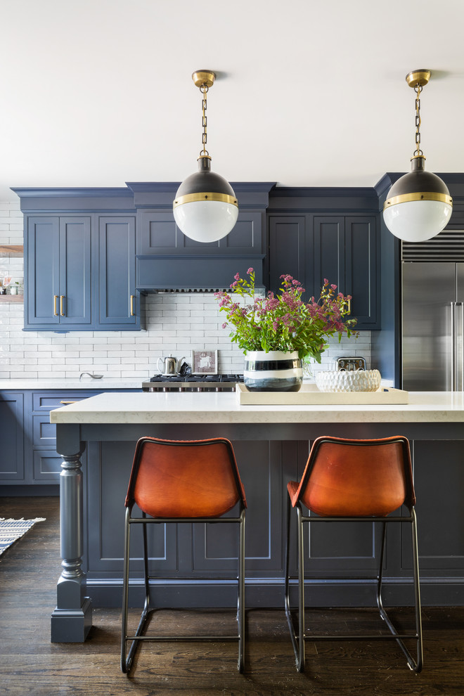 Klassische Wohnküche in L-Form mit Waschbecken, Schrankfronten mit vertiefter Füllung, blauen Schränken, Quarzit-Arbeitsplatte, Küchenrückwand in Weiß, Küchengeräten aus Edelstahl, dunklem Holzboden, Kücheninsel und braunem Boden in New York
