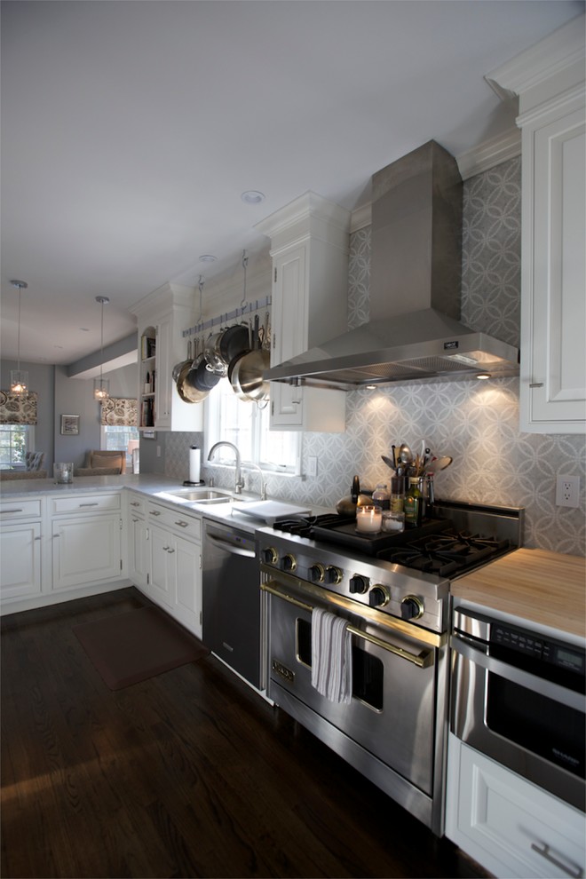 Inredning av ett modernt mellanstort kök, med en dubbel diskho, luckor med upphöjd panel, vita skåp, grått stänkskydd, rostfria vitvaror, mörkt trägolv, en halv köksö och brunt golv