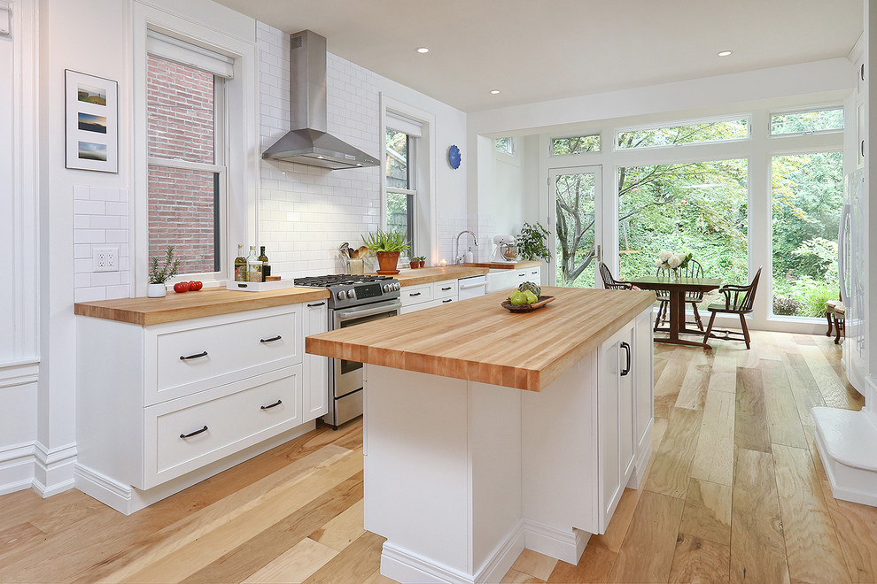 Exempel på ett stort klassiskt linjärt kök och matrum, med en rustik diskho, skåp i shakerstil, vita skåp, träbänkskiva, vitt stänkskydd, stänkskydd i tunnelbanekakel, rostfria vitvaror, mellanmörkt trägolv, en köksö och brunt golv