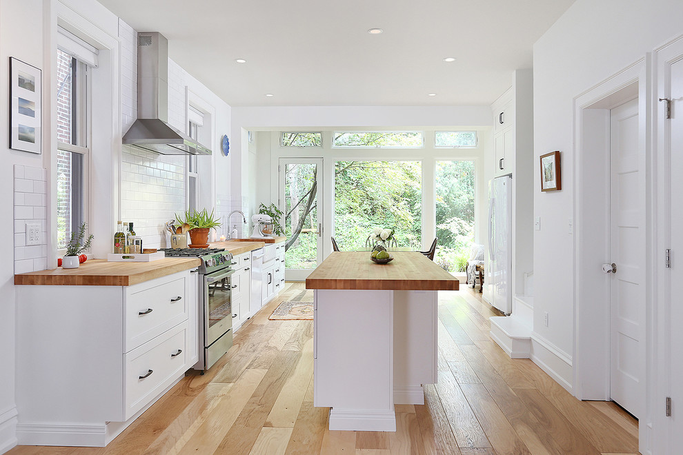 Inspiration for a large classic galley kitchen/diner in Philadelphia with a belfast sink, shaker cabinets, white cabinets, wood worktops, white splashback, metro tiled splashback, stainless steel appliances, medium hardwood flooring, an island and brown floors.