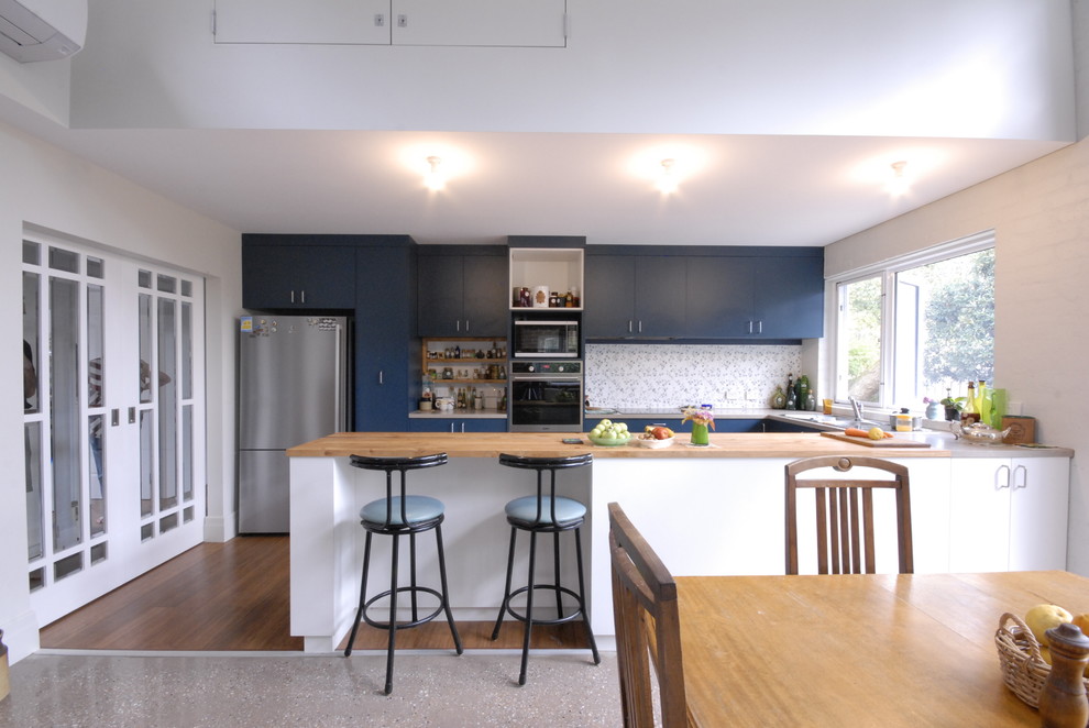 Photo of a medium sized contemporary u-shaped open plan kitchen in Melbourne with a double-bowl sink, beaded cabinets, blue cabinets, wood worktops, multi-coloured splashback, ceramic splashback, stainless steel appliances, concrete flooring, beige floors and multicoloured worktops.