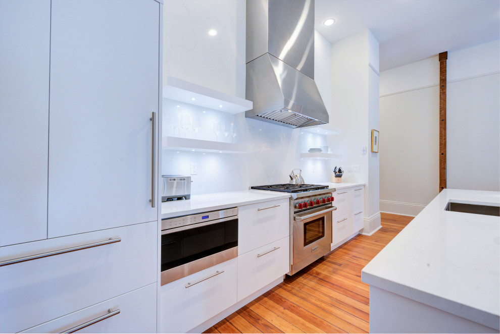 Exempel på ett mellanstort modernt vit vitt kök, med släta luckor, vita skåp, vitt stänkskydd, stänkskydd i porslinskakel, rostfria vitvaror, mellanmörkt trägolv och en köksö
