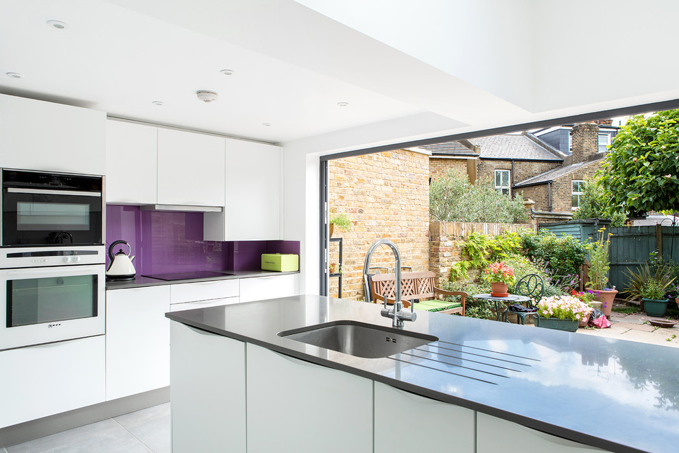 This is an example of a medium sized contemporary enclosed kitchen in London with a submerged sink, flat-panel cabinets, white cabinets, quartz worktops, glass sheet splashback and an island.