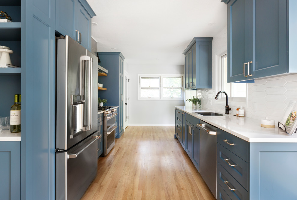 Klassisk inredning av ett mellanstort vit vitt kök, med en undermonterad diskho, luckor med infälld panel, blå skåp, bänkskiva i kvarts, vitt stänkskydd, stänkskydd i cementkakel, rostfria vitvaror och ljust trägolv
