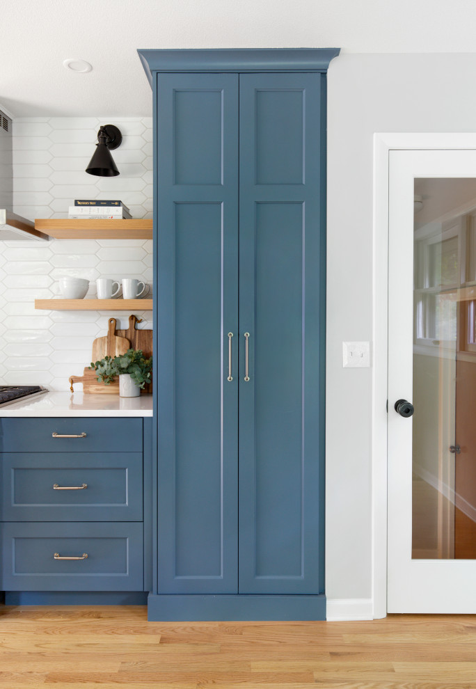 Inredning av ett klassiskt mellanstort vit vitt kök, med en undermonterad diskho, luckor med infälld panel, blå skåp, bänkskiva i kvarts, vitt stänkskydd, stänkskydd i cementkakel, rostfria vitvaror och ljust trägolv