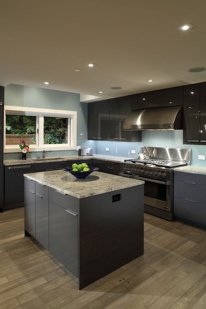 Foto på ett funkis kök, med granitbänkskiva, släta luckor, grå skåp, blått stänkskydd, glaspanel som stänkskydd, mellanmörkt trägolv och brunt golv