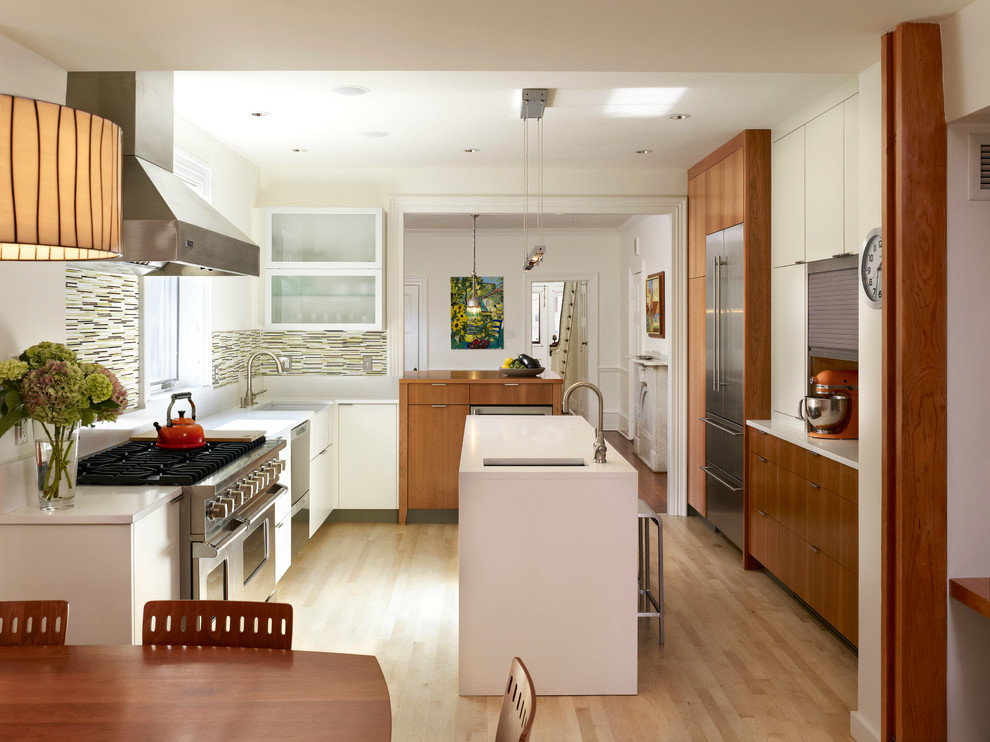 Bild på ett funkis kök, med en rustik diskho, släta luckor, skåp i mellenmörkt trä, bänkskiva i kvarts, flerfärgad stänkskydd, stänkskydd i glaskakel, rostfria vitvaror, ljust trägolv och en köksö