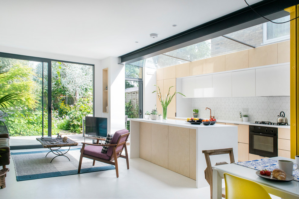 Midcentury galley kitchen in London with flat-panel cabinets, light wood cabinets, white splashback, black appliances, an island and grey floors.