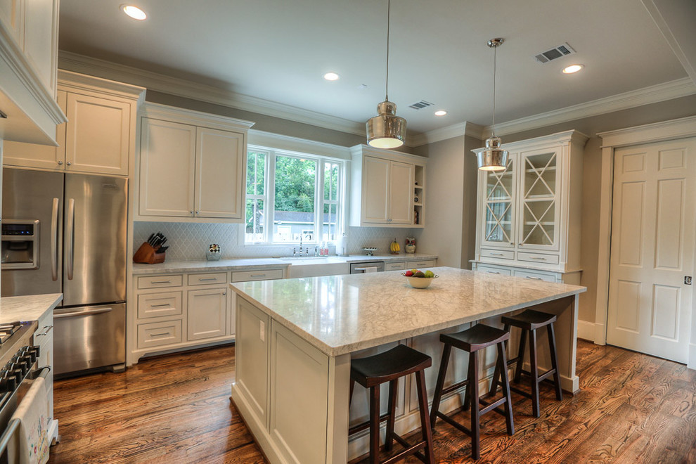Example of a large arts and crafts u-shaped medium tone wood floor kitchen pantry design in Houston with a farmhouse sink, shaker cabinets, white cabinets, marble countertops, gray backsplash, ceramic backsplash, stainless steel appliances and an island