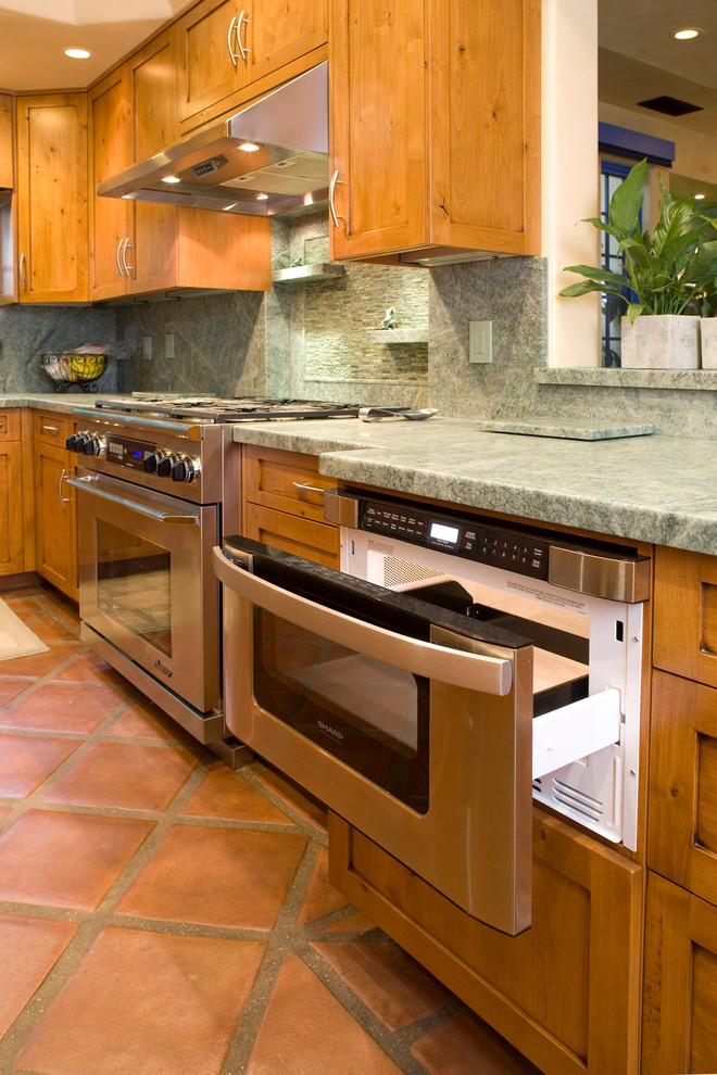 Bild på ett avskilt eklektiskt u-kök, med en integrerad diskho, skåp i shakerstil, skåp i mellenmörkt trä, grönt stänkskydd, stänkskydd i stenkakel, integrerade vitvaror, klinkergolv i terrakotta och granitbänkskiva
