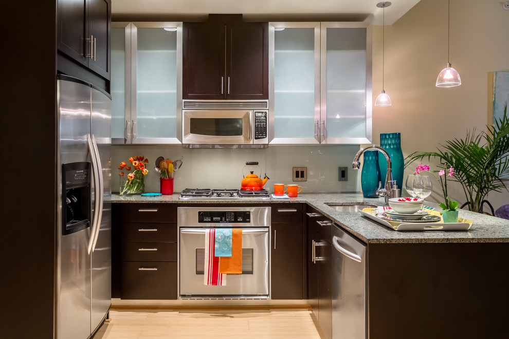 Bild på ett litet funkis kök, med en undermonterad diskho, luckor med glaspanel, svarta skåp, granitbänkskiva, grönt stänkskydd, glaspanel som stänkskydd, rostfria vitvaror, bambugolv, en halv köksö och gult golv