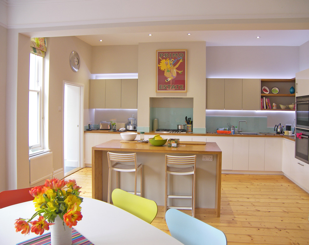 Cette image montre une cuisine design avec un placard à porte plane, des portes de placard blanches, un plan de travail en bois, une crédence bleue, un sol en bois brun et îlot.