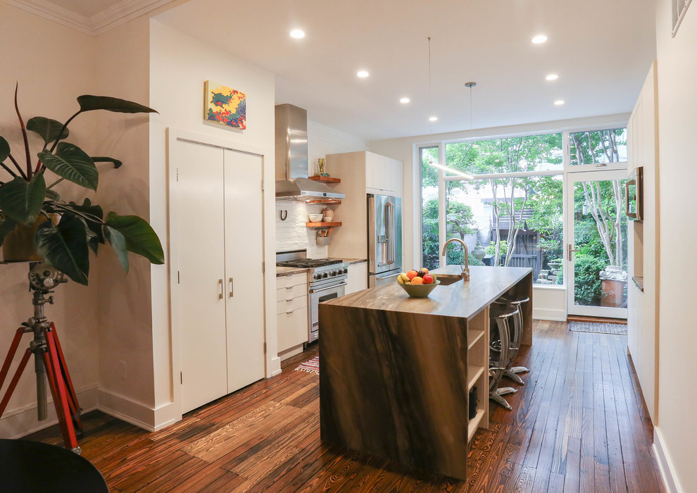 Photo of a contemporary galley kitchen/diner in Baltimore with flat-panel cabinets, granite worktops, white splashback, brick splashback, stainless steel appliances, medium hardwood flooring, an island and multi-coloured floors.