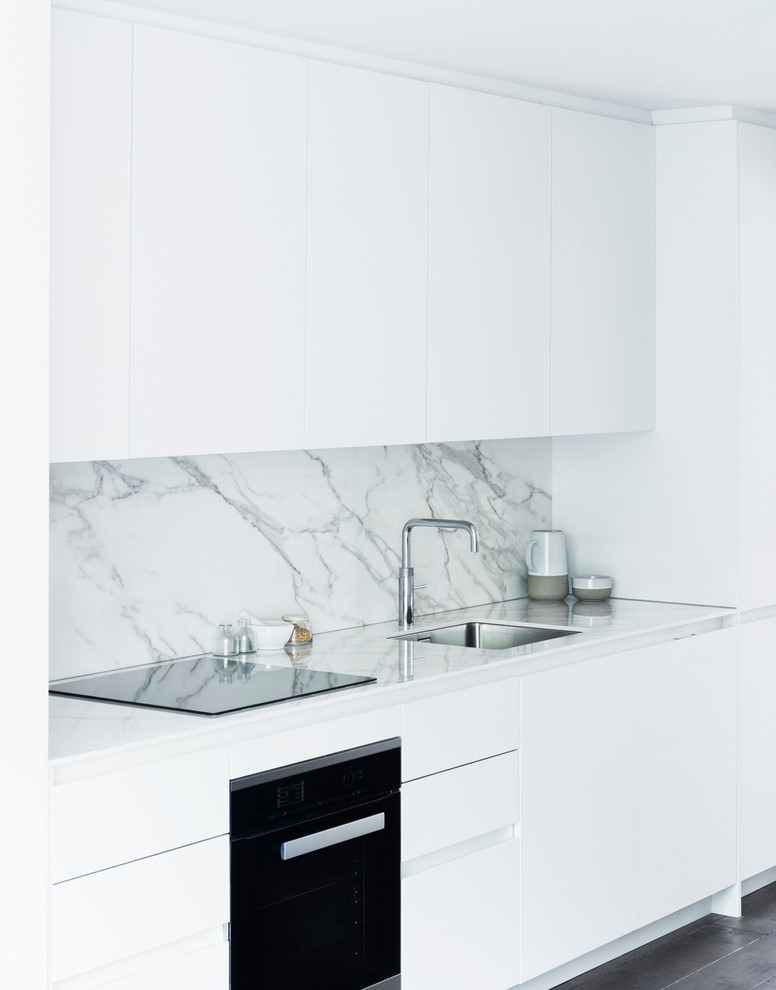 Offene, Zweizeilige, Mittelgroße Moderne Küche ohne Insel mit integriertem Waschbecken, weißen Schränken, Mineralwerkstoff-Arbeitsplatte, Elektrogeräten mit Frontblende und dunklem Holzboden in London