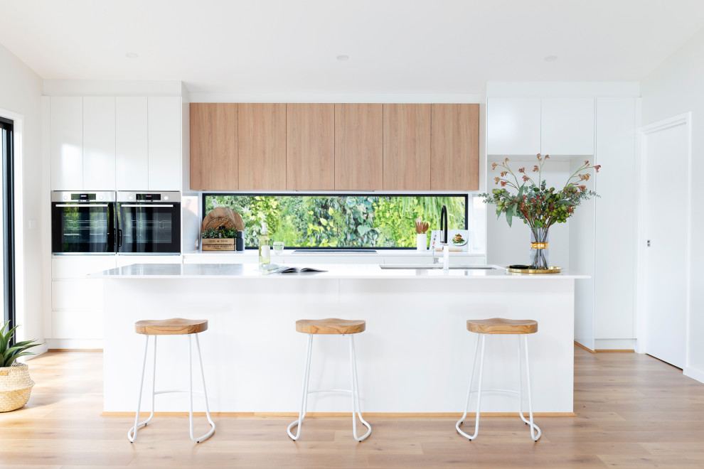 Immagine di una cucina design con lavello sottopiano, ante bianche, top in quarzo composito, paraspruzzi a finestra, elettrodomestici neri, pavimento in laminato e top bianco