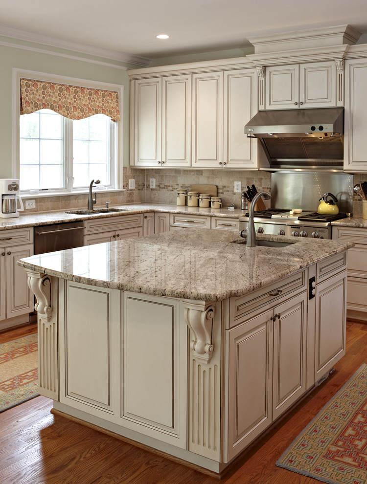 This is an example of a large traditional l-shaped enclosed kitchen in DC Metro with stainless steel appliances, granite worktops, raised-panel cabinets, beige cabinets, a double-bowl sink, brown splashback, stone tiled splashback, medium hardwood flooring, an island, brown floors and beige worktops.