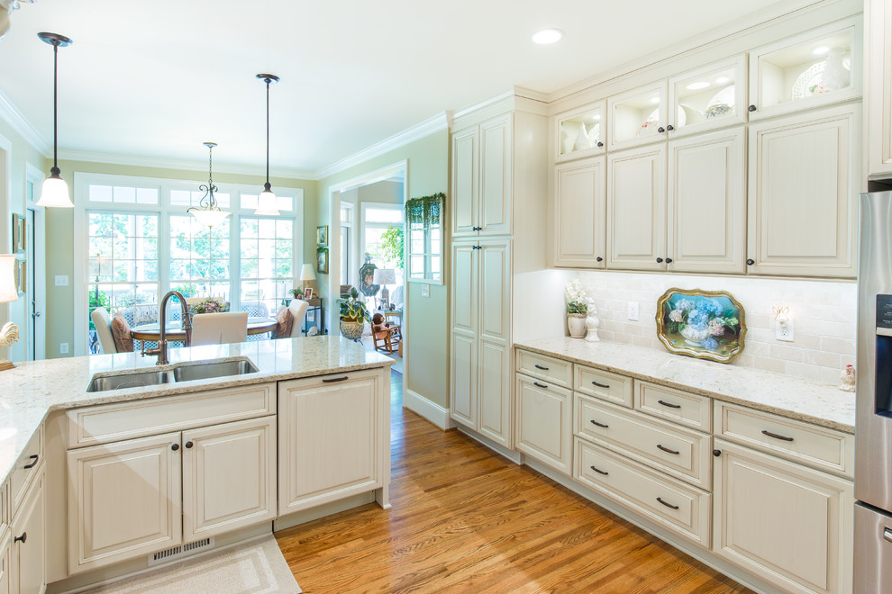Exempel på ett mellanstort klassiskt kök, med en undermonterad diskho, luckor med upphöjd panel, vita skåp, granitbänkskiva, beige stänkskydd, stänkskydd i keramik, rostfria vitvaror, mellanmörkt trägolv och en halv köksö