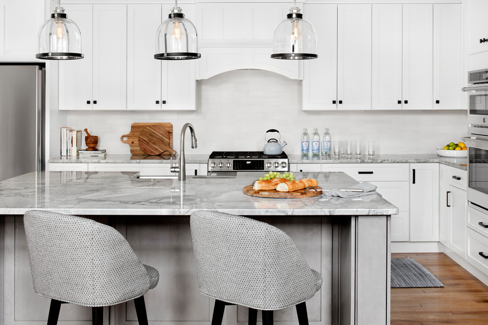 Klassische Küche in L-Form mit Schrankfronten im Shaker-Stil, weißen Schränken, Küchenrückwand in Weiß, Küchengeräten aus Edelstahl, braunem Holzboden, Kücheninsel, braunem Boden und grauer Arbeitsplatte in Baltimore