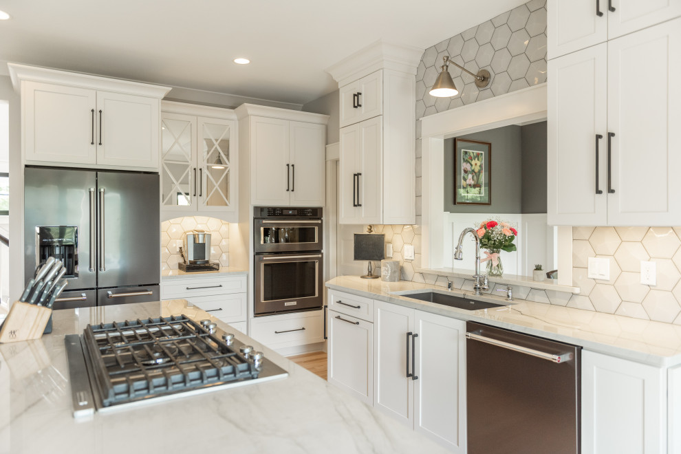 Inspiration for a classic l-shaped kitchen in Milwaukee with a submerged sink, shaker cabinets, white cabinets, white splashback, stainless steel appliances, medium hardwood flooring, an island, brown floors and white worktops.