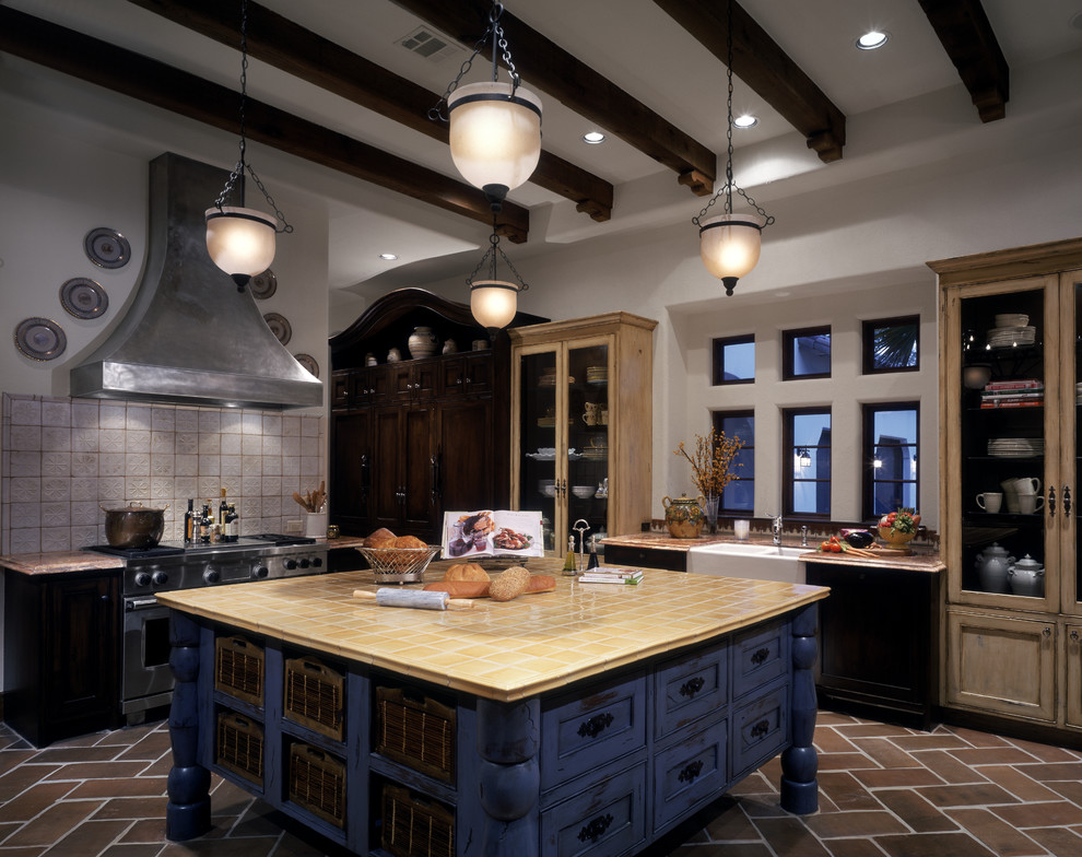 This is an example of an expansive eclectic u-shaped kitchen/diner in Houston with a belfast sink, beaded cabinets, distressed cabinets, tile countertops, stainless steel appliances, terracotta flooring and an island.