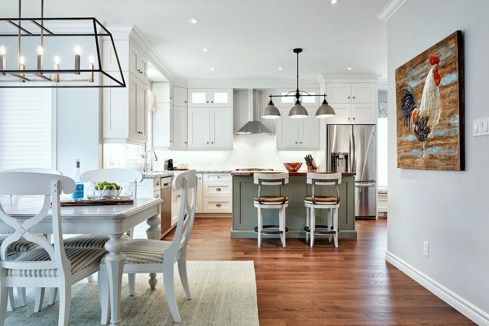 Large transitional medium tone wood floor kitchen photo in Toronto with a farmhouse sink, shaker cabinets, white cabinets, granite countertops, white backsplash, subway tile backsplash, stainless steel appliances and an island