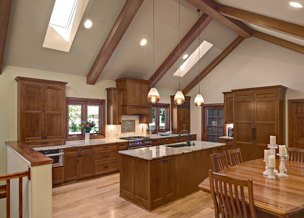 Eat-in kitchen - large traditional l-shaped light wood floor eat-in kitchen idea in Minneapolis with an undermount sink, flat-panel cabinets, medium tone wood cabinets, granite countertops, beige backsplash, stone tile backsplash, paneled appliances and an island