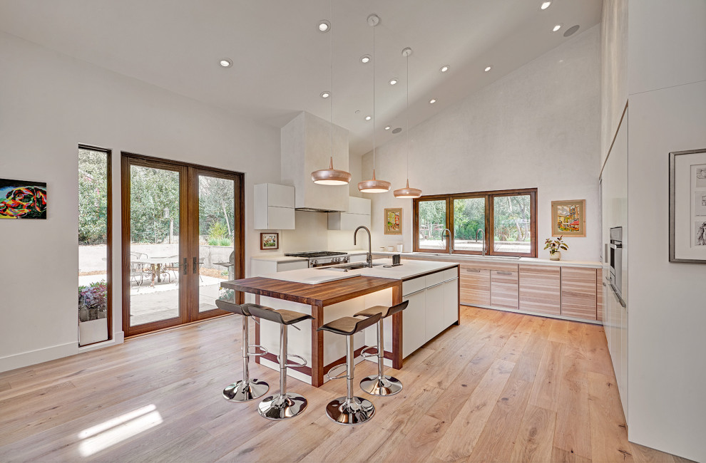 Expansive contemporary u-shaped kitchen/diner in Sacramento with a submerged sink, flat-panel cabinets, white cabinets, engineered stone countertops, white splashback, stainless steel appliances, light hardwood flooring, an island, multi-coloured floors, white worktops and a vaulted ceiling.