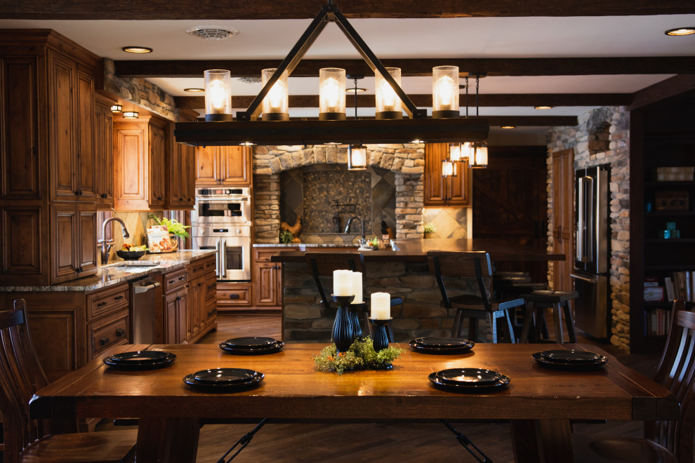 Photo of an expansive rustic l-shaped kitchen/diner in Other with a submerged sink, raised-panel cabinets, medium wood cabinets, grey splashback, stone tiled splashback, stainless steel appliances, an island, brown floors, grey worktops and exposed beams.