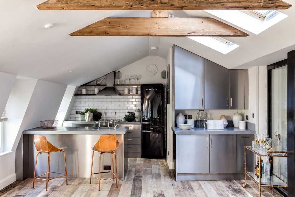 Inspiration for a small industrial galley kitchen in London with flat-panel cabinets, stainless steel cabinets, white splashback, metro tiled splashback, black appliances and a breakfast bar.