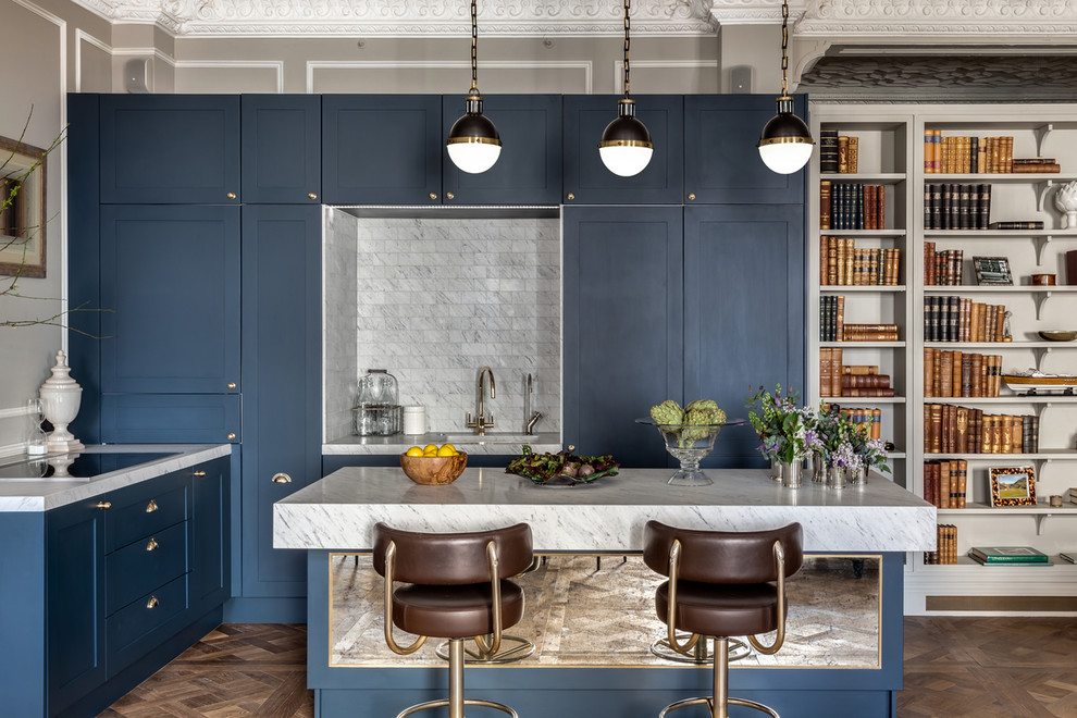 Aménagement d'une cuisine américaine classique avec un placard à porte shaker, îlot, des portes de placard bleues, plan de travail en marbre, une crédence grise, une crédence en carrelage de pierre, un évier encastré et un sol en bois brun.